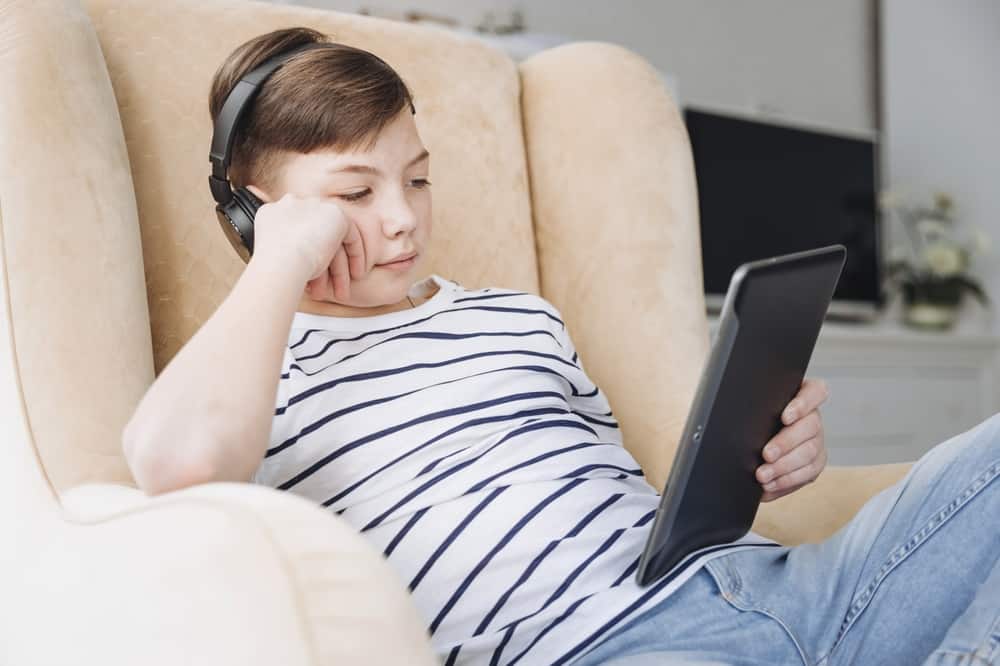 A young boy in a chair using a tablet with headphones on