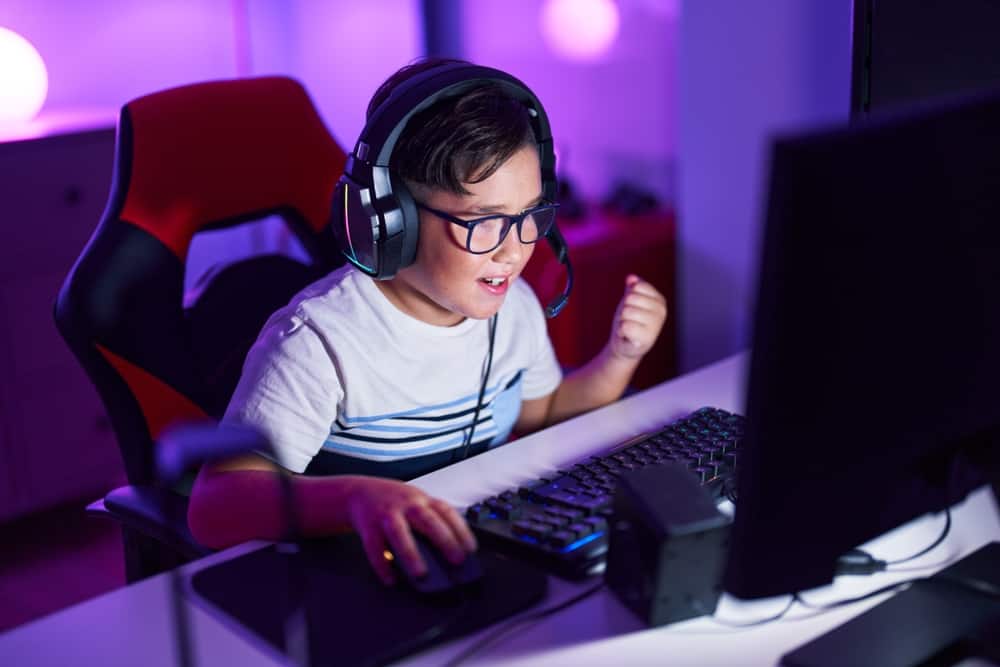A young boy playing a computer game at his desk wearing a gaming headset