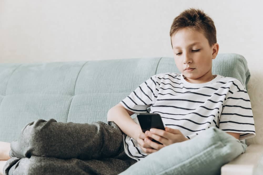 A young boy sitting on a couch, looking at a smartphone