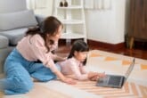 A parent and child on the living room floor using a laptop