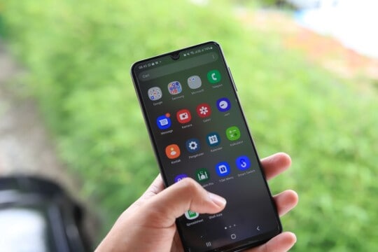 A person holding an Android phone with apps on the screen