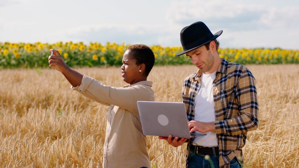 A man using a laptop and a woman taking a photo in a rural area