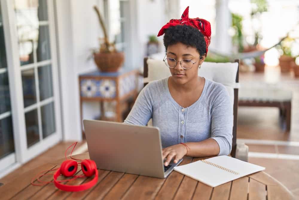 A young woman sits at a table while typing on her laptop.