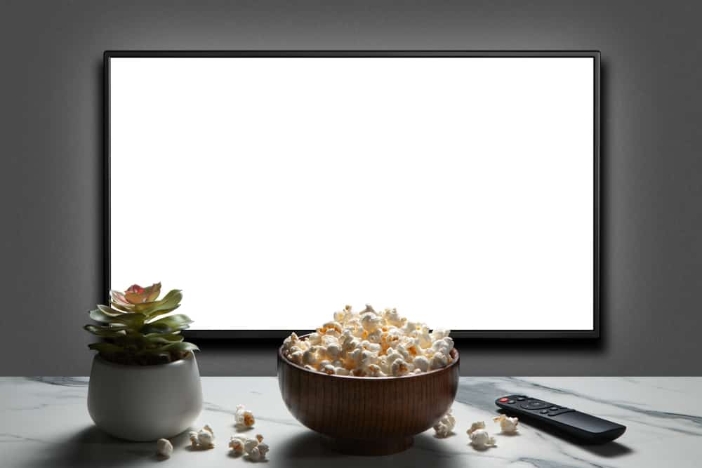 A flat-screen TV on a gray wall with a succulent pot, a bowl of popcorn, and a remote control on a marble counter