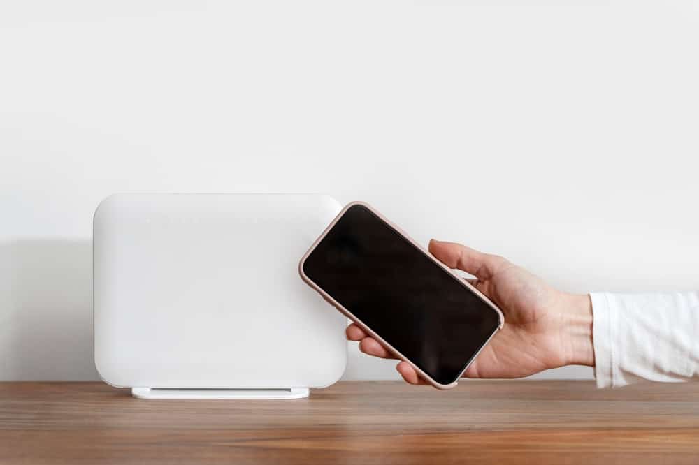 A hand holding a phone next to a router 