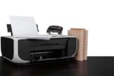 A bulky printer on a black table with office supplies around and on it
