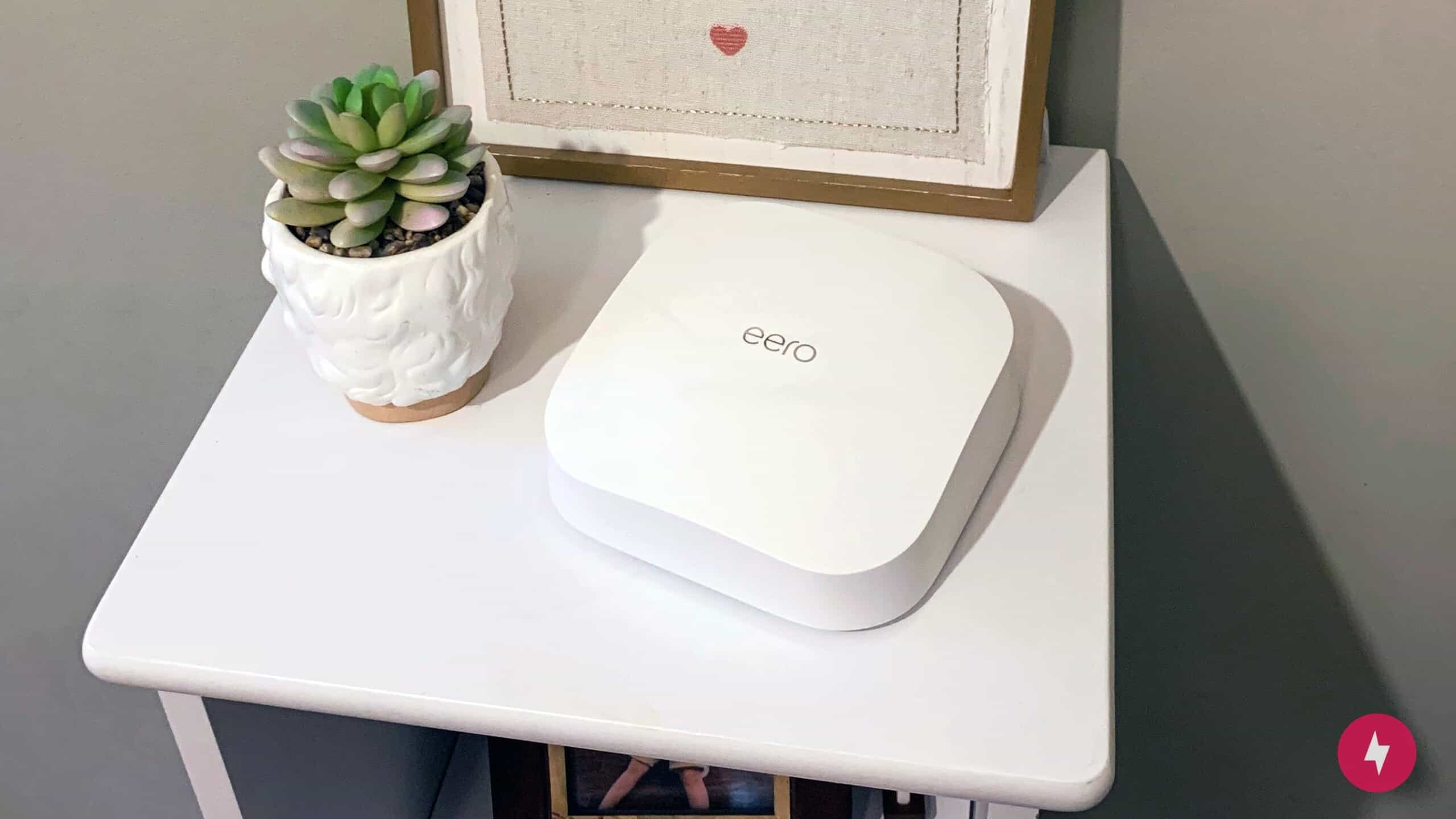 An eero Pro 6 router sits on a table with a succulent plant and a portrait.