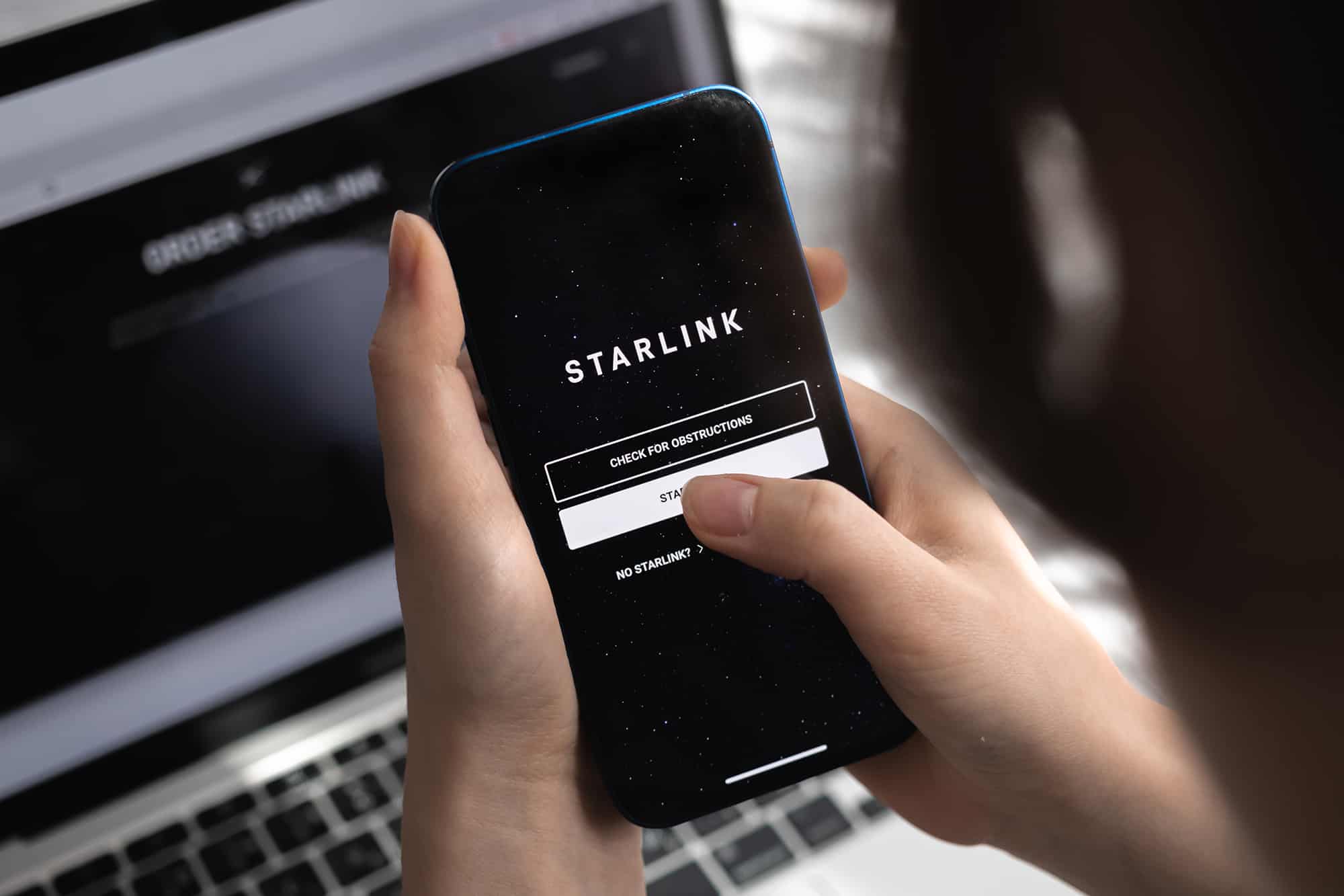 Woman using the Starlink app on her phone in front of a laptop