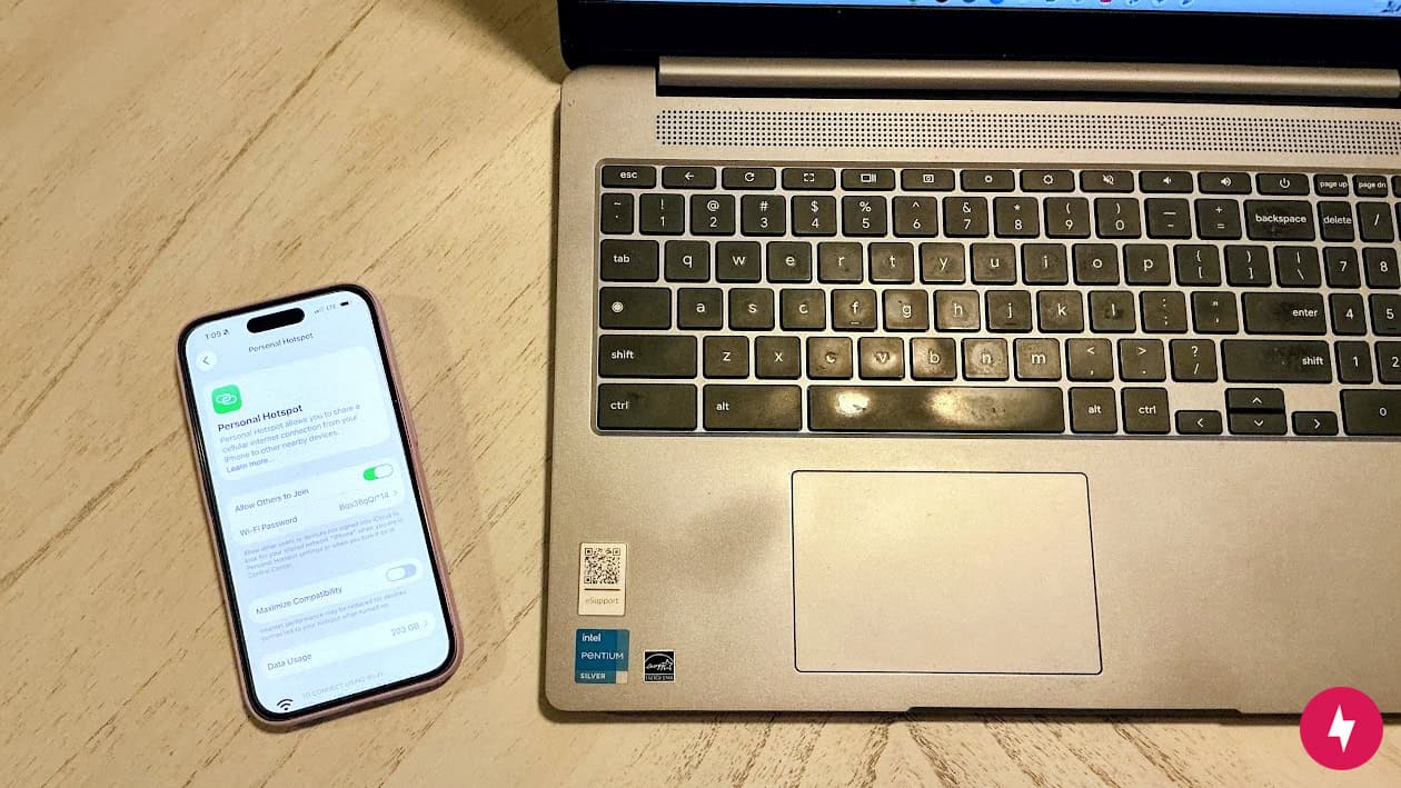 An iPhone 16 open on Personal Hotspot beside an open laptop at a cafe.