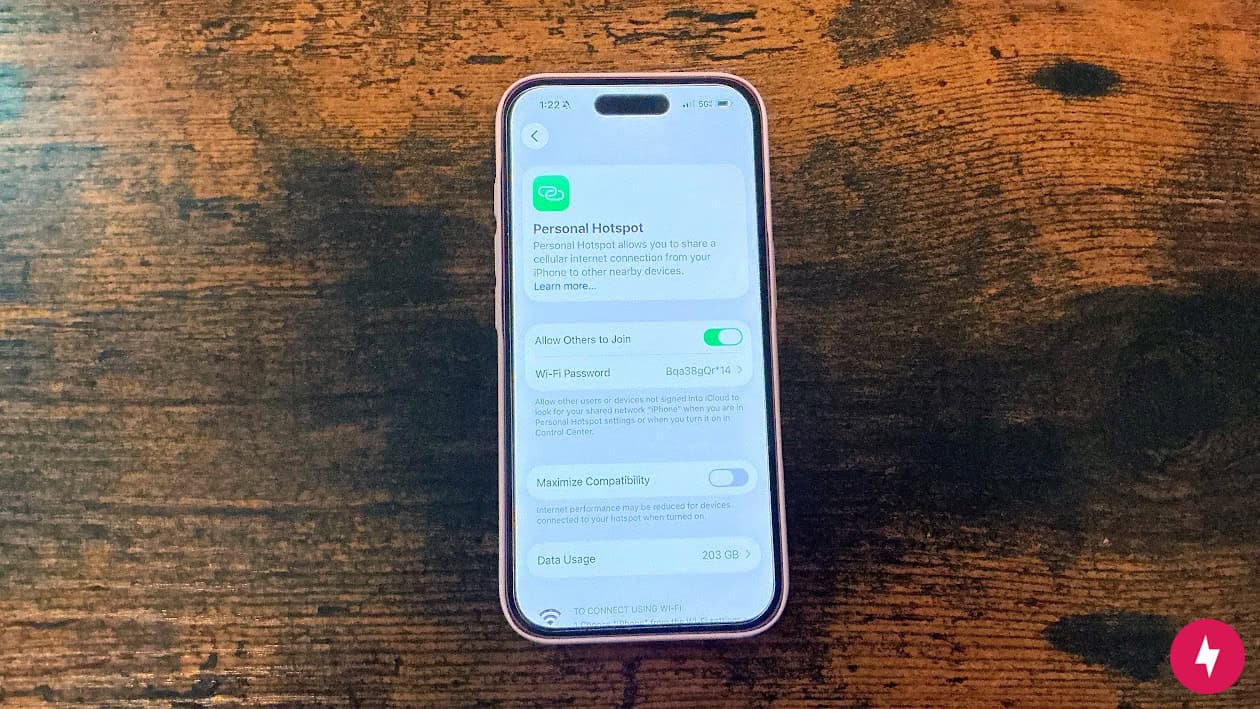 An iPhone 16 on the Personal Hotspot screen on a wooden desk.