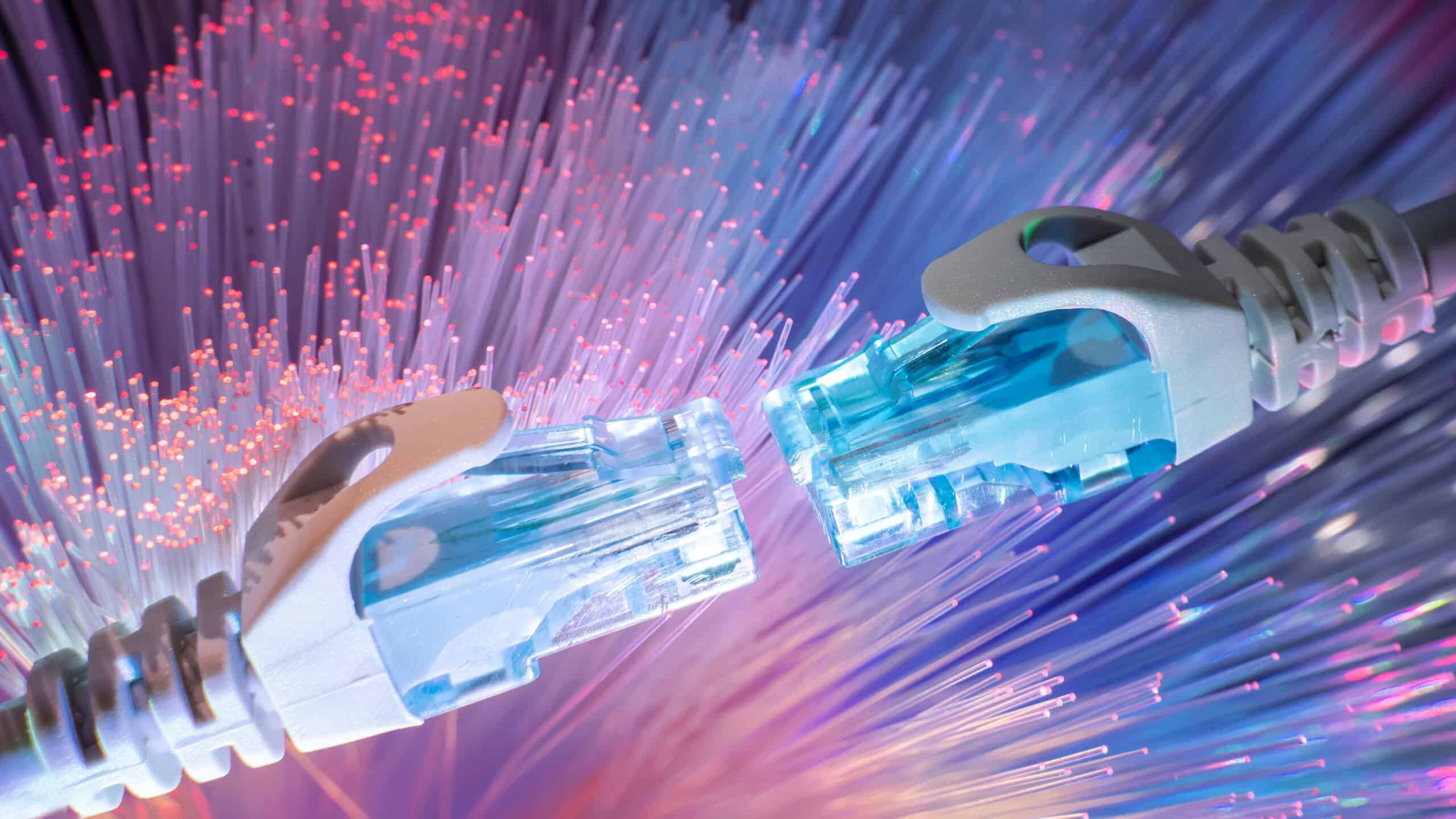 Two Ethernet cables almost touch each other with a background of fiber-optic cables.