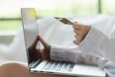 A woman holding a credit card while using a laptop in this image from Shutterstock.