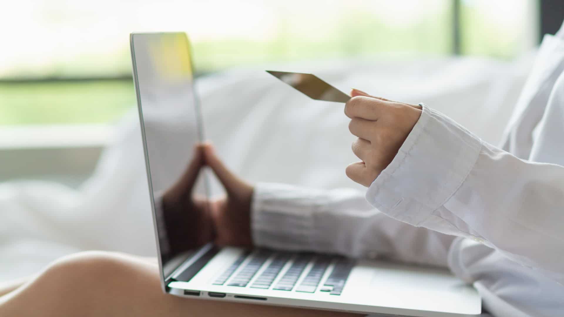 A woman holding a credit card while using a laptop in this image from Shutterstock.