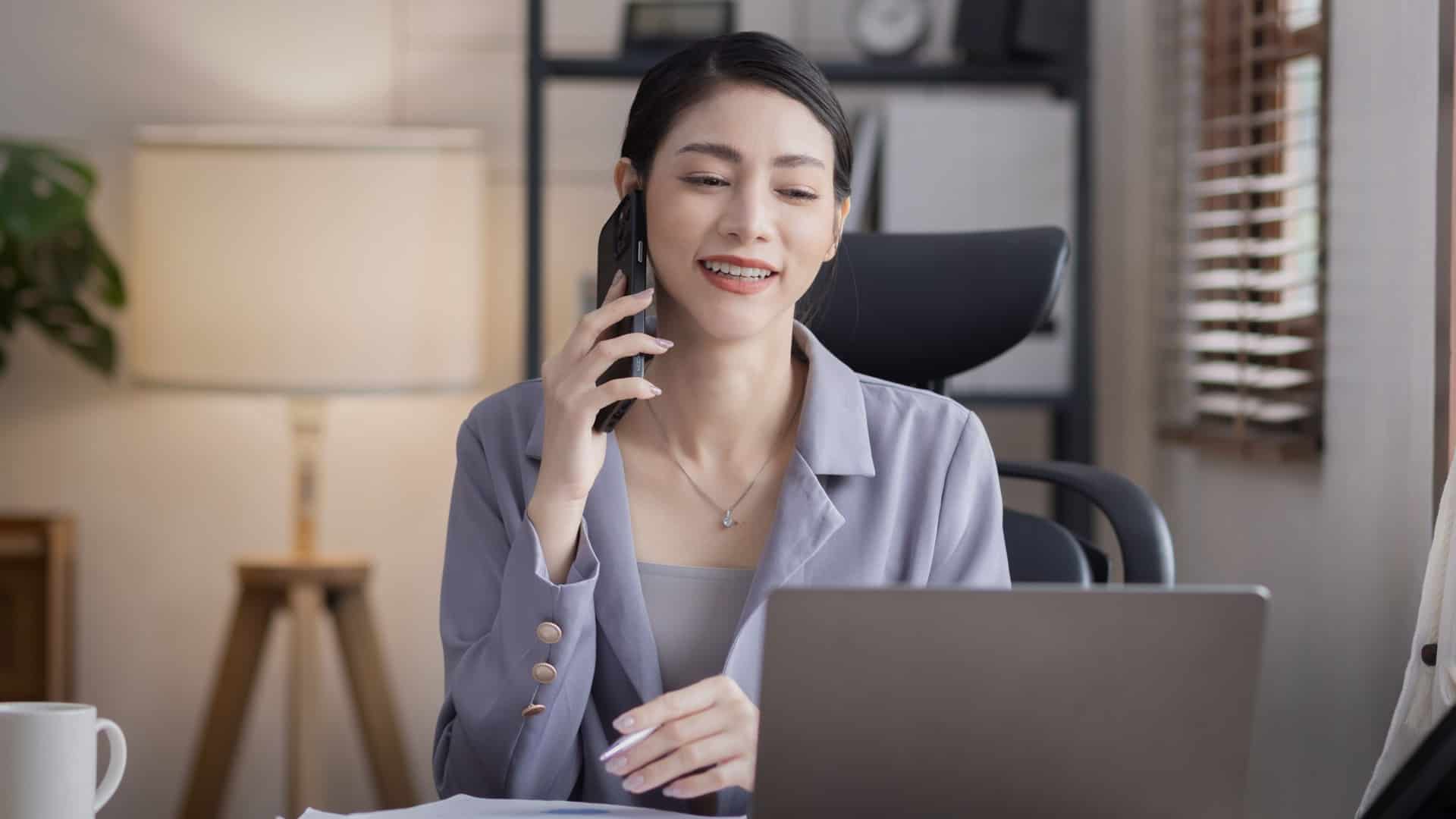  A woman talks on the phone while looking at a laptop in this image from Shutterstock.