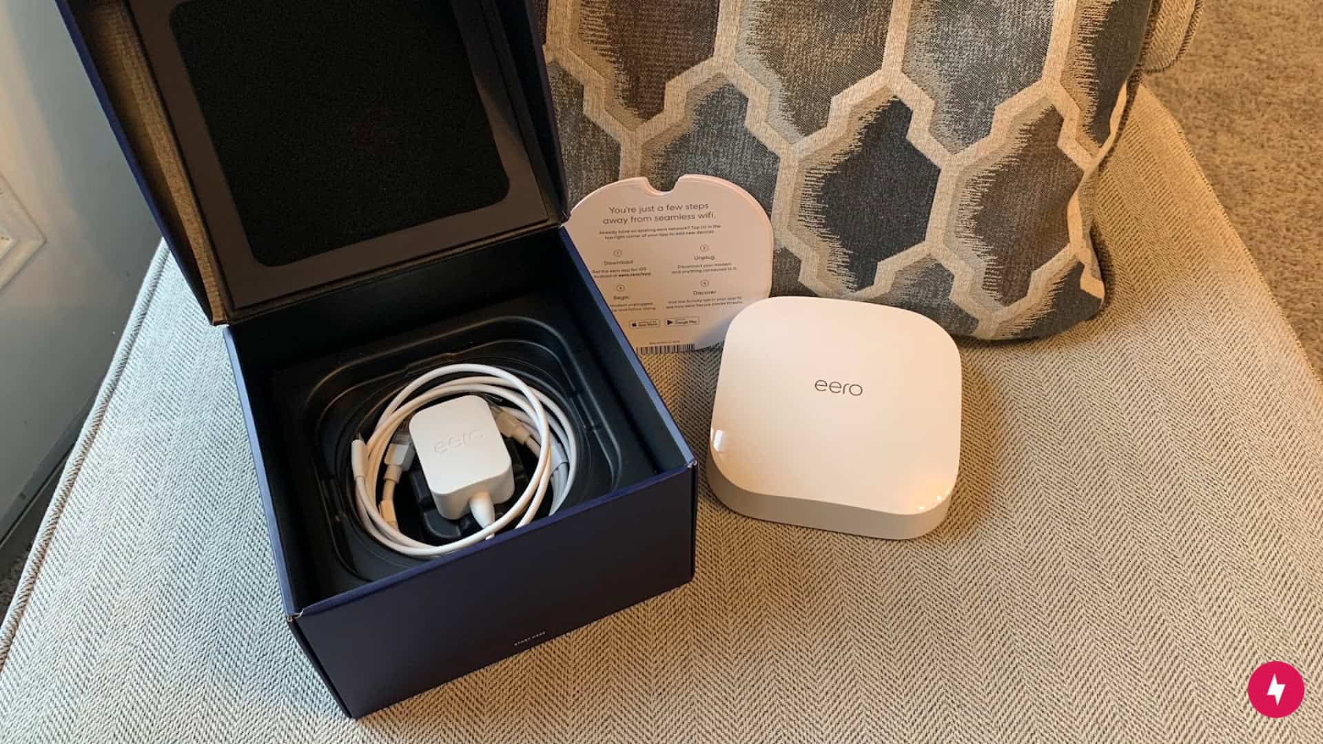 An open box of cords, instructions, and an Eero device.