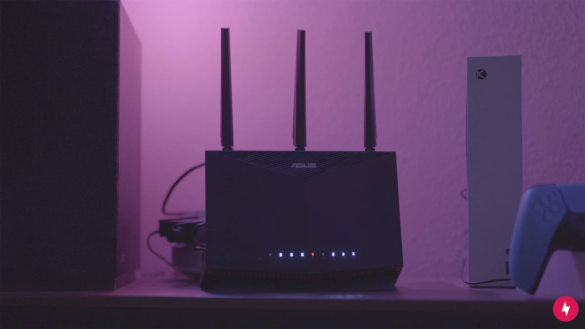 Asus RT-AX86U Pro router sitting on a table beside an Xbox Series S and a controller with a pink light in the background