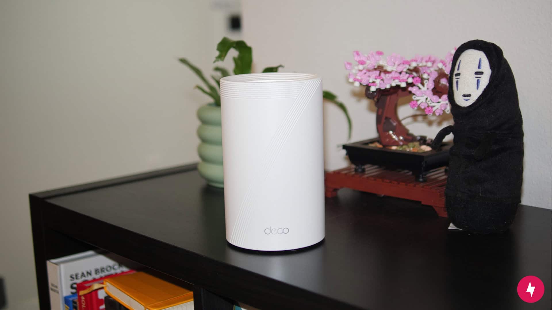 The TP-Link Deco BE63 placed on a black shelf next to decorative items.
